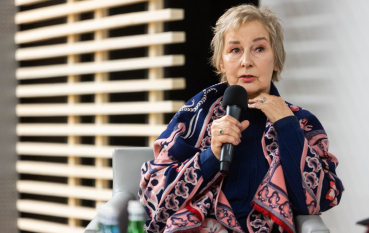 60-letnia kobieta z jasnymi, krótkimi włosami, ubrana w kolorowy sweter.