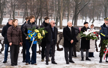 Grupa osób , trzy osoby trzymają wiązankę; pierwsza od lewej kobieta i młody mężczyzna trzymający w ręku wiązankę żółto-niebieską 