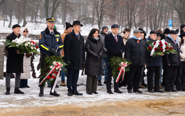 Grupa osób, cztery osoby z biało-czerwonymi wiązankami, w grupie byli więźniowie. 