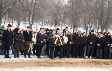 Grupa osób, dwie osoby trzymają w rękach wiązanki.