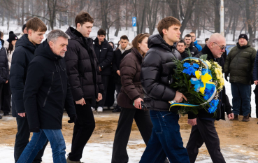 Kobieta, dwóch starszych i trzech młodych mężczyzn składają kwiaty.