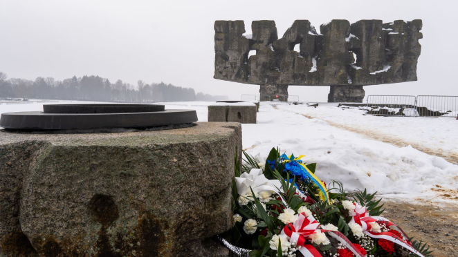 Na pierwszym planie wiązanki kwiatów wsparte o kamienny znicz, na drugim planie Pomnik-Brama