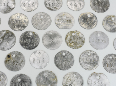 Kilkadziesiąt metalowych okrągłych blaszek z dziurkami na górze i wybitymi numerami