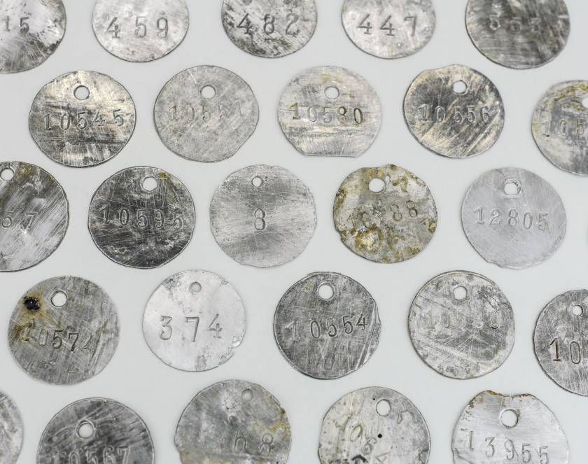 Kilkadziesiąt metalowych okrągłych blaszek z dziurkami na górze i wybitymi numerami