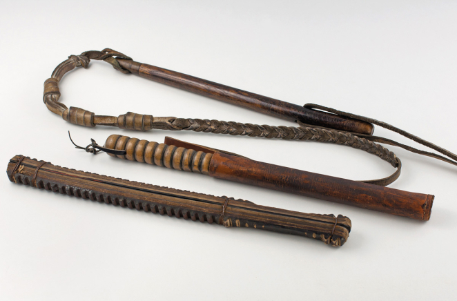 Two sticks made of grooved wood and a leather whip on a neutral background