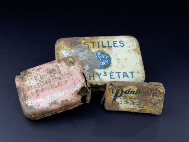 Trzy metalowe opakowania po lekach z nieczytelnymi napisami