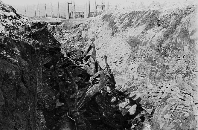 Rów ziemny, na jego dnie metalowe pokrzywione podwozia samochodowe