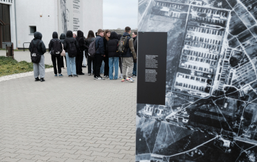 Grupa młodych osób przez Centrum Obsługi Zwiedzających, na pierwszym planie fragment panelu wystawy prezentującej zdjęcie lotnicze obozu koncentracyjnego na Majdanku z 1944 roku  