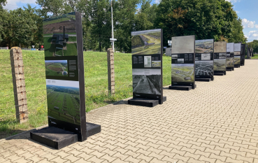 Kilka paneli wystawy, na drugim planie ogrodzenie z drutów kolczastych 