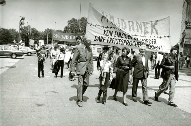 Grupa ludzi idzie ulicą, trzymając transparent z napisem w języku niemieckim