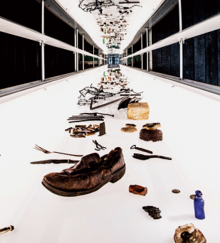 Podniesione wieko szklanej gabloty ukazujące przedmioty, na pierwszym planie męski but 