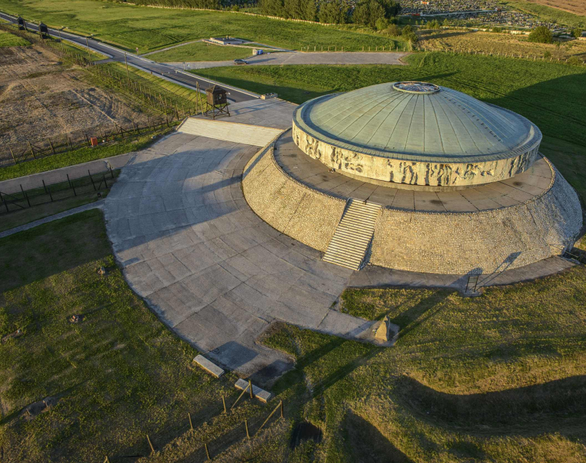 Zdjęcie z lotu ptaka pokazujące Mauzoleum na Majdanku - betonowy pomnik z okrągłą kopułą. Dookoła tereny zielone