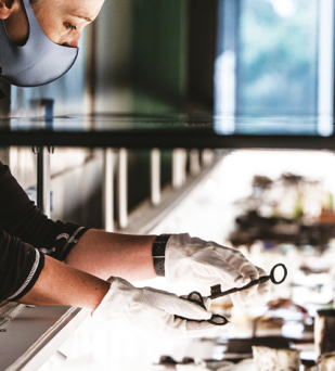 Kobieta w maseczce  i białych bawełnianych rękawiczkach trzyma w dłoniach stary klucz, dookoła przedmioty