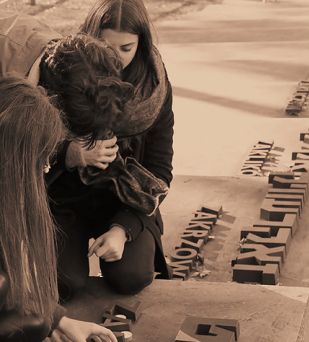 Grupa młodych osób klęczących na stopniach, obok napisy w języku polskim i hebrajskim lubelskich miast 