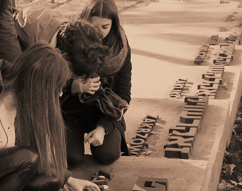 Grupa młodych osób klęczących na stopniach, obok napisy w języku polskim i hebrajskim lubelskich miast