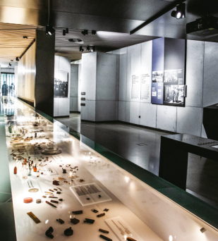 Wnętrze wystawy , na pierwszym planie podświetlona gablota z przedmiotami, na drugim plansze wystawy o treściach historycznych 