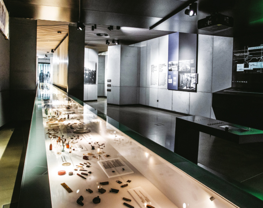 Wnętrze wystawy , na pierwszym planie podświetlona gablota z przedmiotami, na drugim plansze wystawy o treściach historycznych