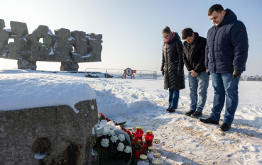 Kobieta i dwóch mężczyzn ubranych w zimowe kurtki składa hołd pod Pomnikiem Bramą.