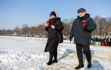 Kobieta i mężczyzna ubrani w zimowe kurtki niosą czerwone znicze.