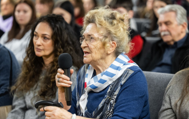 Starsza kobieta w chuście w biało-niebieskie pasy przemawia do mikrofonu