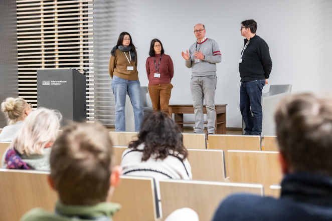 Dwóch mężczyzn i dwie kobiety przemawia na scenie w sali audytoryjnej. 