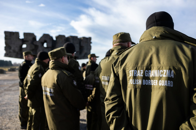 Grupa mężczyzn stojąca tyłem, napis na mundurze: Straż Graniczna, Polish border guard 