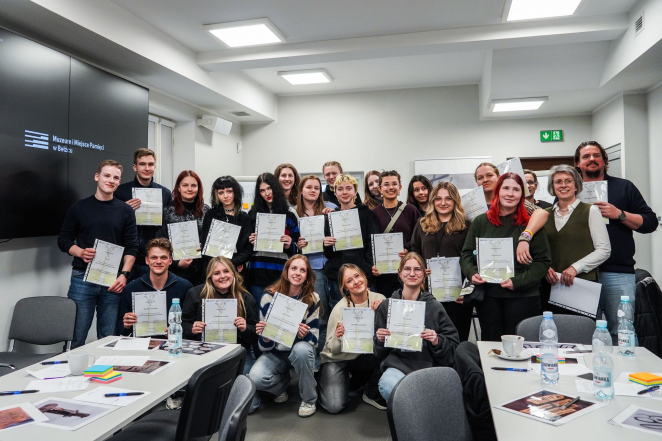 Grupa kilkunastu młodych osób w sali trzymających w rękach dyplomy. 
