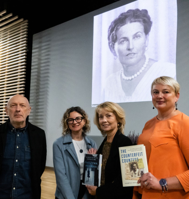 Trzy kobiety oraz łysy mężczyzna na tle prezentacji z czarno-białym zdjęciem kobiety o upiętych włosach. 