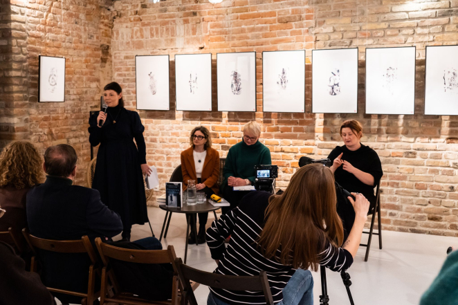 Cztery kobiety na sali, kobieta w czarnej sukience przemawia do mikrofonu, kobieta po lewej- tłumaczka PJM