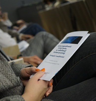 Kobieta trzymająca na kolanach ulotkę seminarium, treść nieczytelna. 