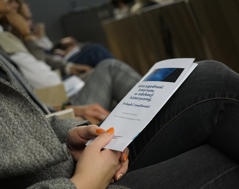 Kobieta trzymająca na kolanach ulotkę seminarium, treść nieczytelna. 