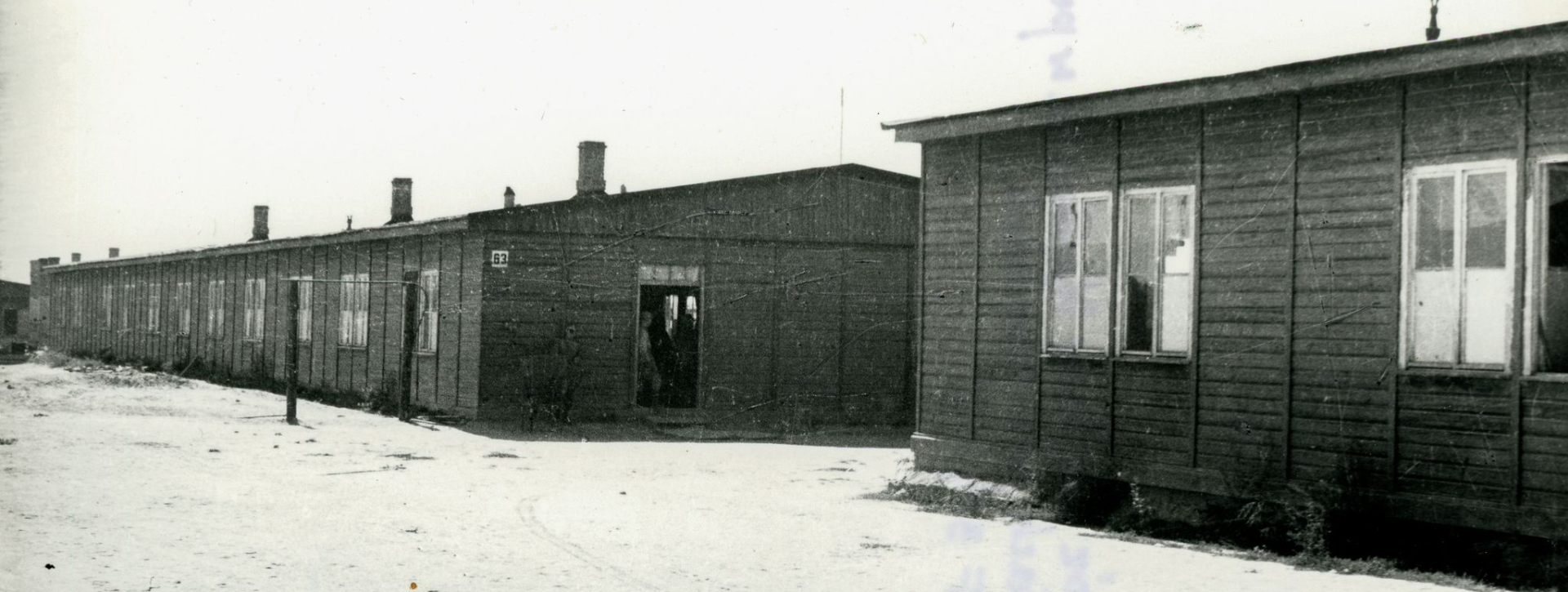 Dwa baraki więźniarskie z oknami, drugi barak z drzwiami otwartymi szeroko 