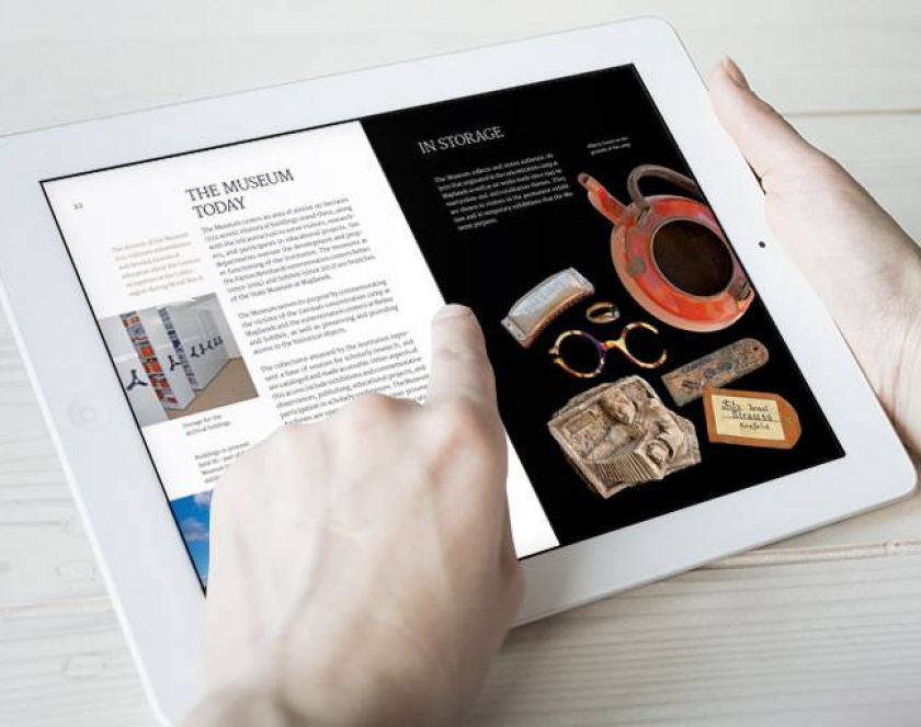 Kobiece dłonie trzymające w ręku tablet z informacją w języku angielskim dotyczącą muzeum oraz zdjęciami obiektów muzealnych 