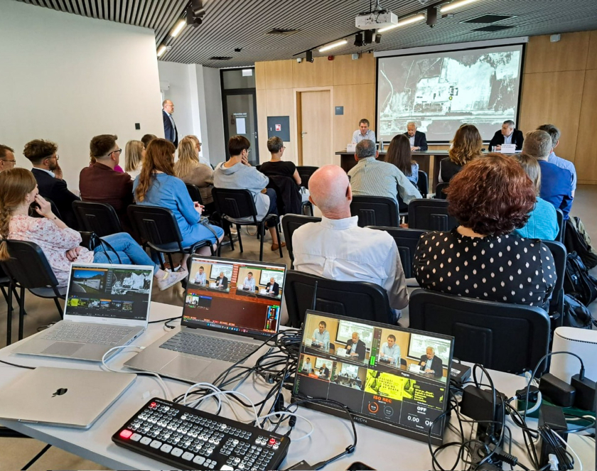 Grupa osób w sali edukacyjnej podczas słuchania debaty, na pierwszym planie laptopy oraz sprzęt elektroniczny służący do transmisji na żywo 