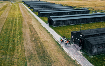 Zdjęcie z drona, rzędy baraków więźniarskich oraz grupa osób przemieszczająca się po ścieżce 