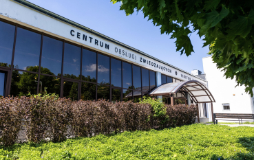 Wejście do Centrum Obsługi Zwiedzających, przeszklona ściana, półokrągły daszek przed wejściem oraz duży napis: Centrum Obsługi Zwiedzających 