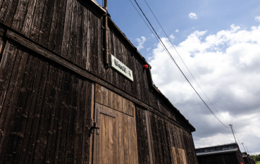 Front drewnianego baraku więźniarskiego, nad drzwiami tabliczka z napisem Block 1 oraz linie napięcia