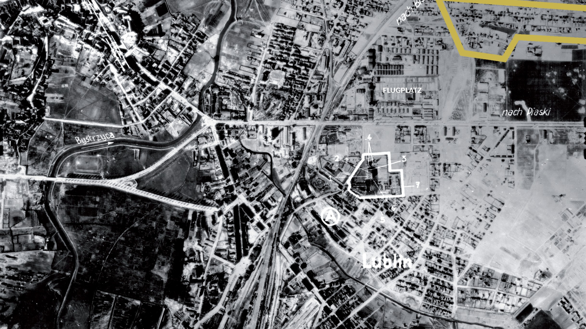Czarno-białe zdjęcie lotnicze przestawiające sieć ulic, zabudowań i pół.