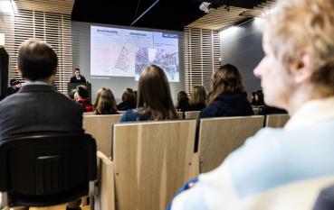 Grupa osób na sali audytoryjnej, na drugim planie prezentacja 
