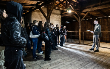 Grupa młodzieży i przewodnik we wnętrzu baraku Łaźni żeńskiej