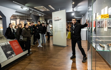 Grupa młodzieży i przewodnik na wystawie; na pierwszym planie przeszklona gablota