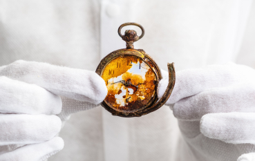 Zniszczona tarcza zegarka kieszonkowego trzymana w dłoniach w białych rękawiczkach