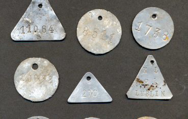 Zbiór dziesięciu metalowych blaszek z wybitymi numerami, część okrągła część trójkątna.