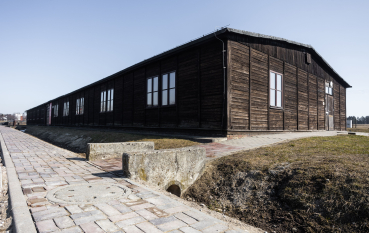 Drewniany barak, na pierwszym planie widoczny betonowy pojazd