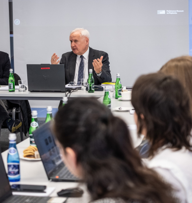 Grupa osób ubranych elegancko siedzących przy stołach. 