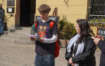 Młody mężczyzna czytający fragment relacji oraz kobieta w średnim wieku. 