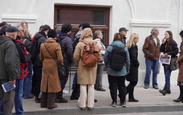 Grupa kilkudziesięciu osób stojąca na chodniku przed kamienicą. 