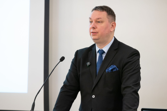 Mężczyzna w średnim wieku w garniturze przemawia do mikrofonu.