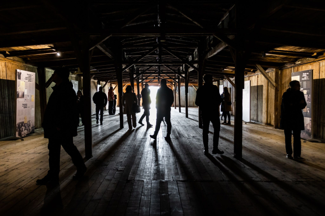 Grupa osób w ciemnym, drewnianym baraku.