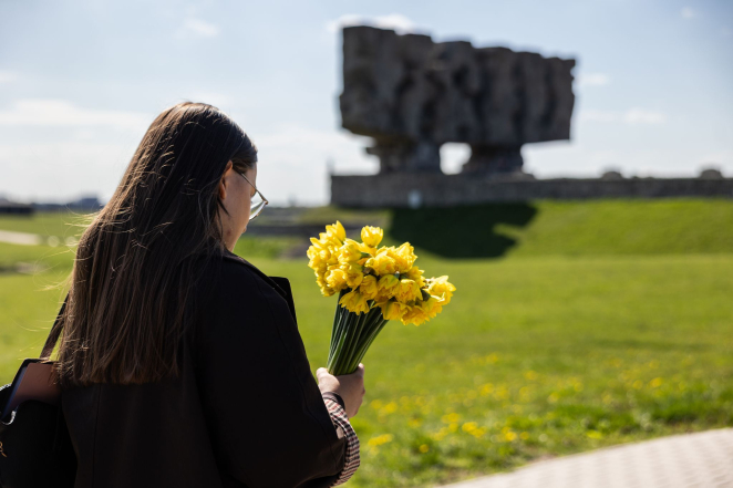 Młoda kobieta z bukietem żonkili, w tle Pomnik Brama. 